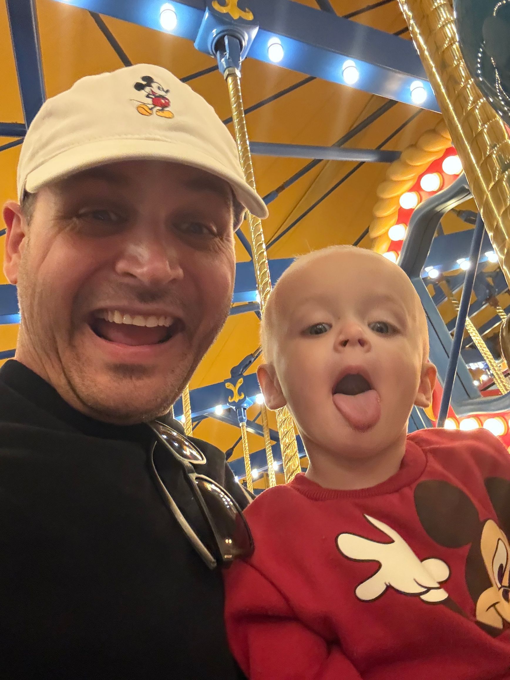 Smiling adult and child posing in a brightly lit amusement ride, child sticking out tongue