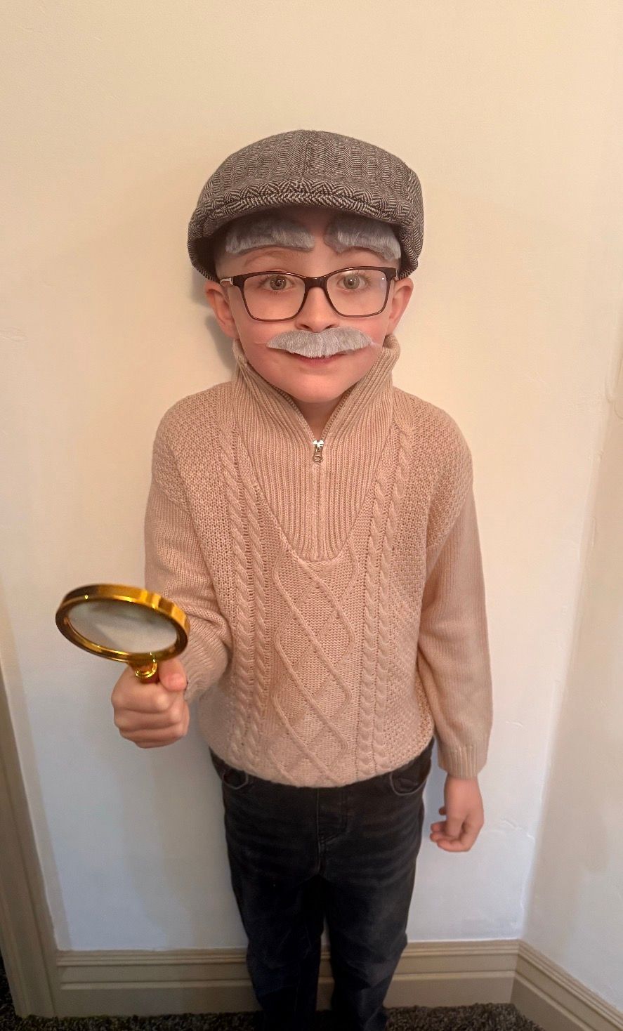 Person in a gray cap and glasses, wearing a pink sweater, holding a magnifying glass.