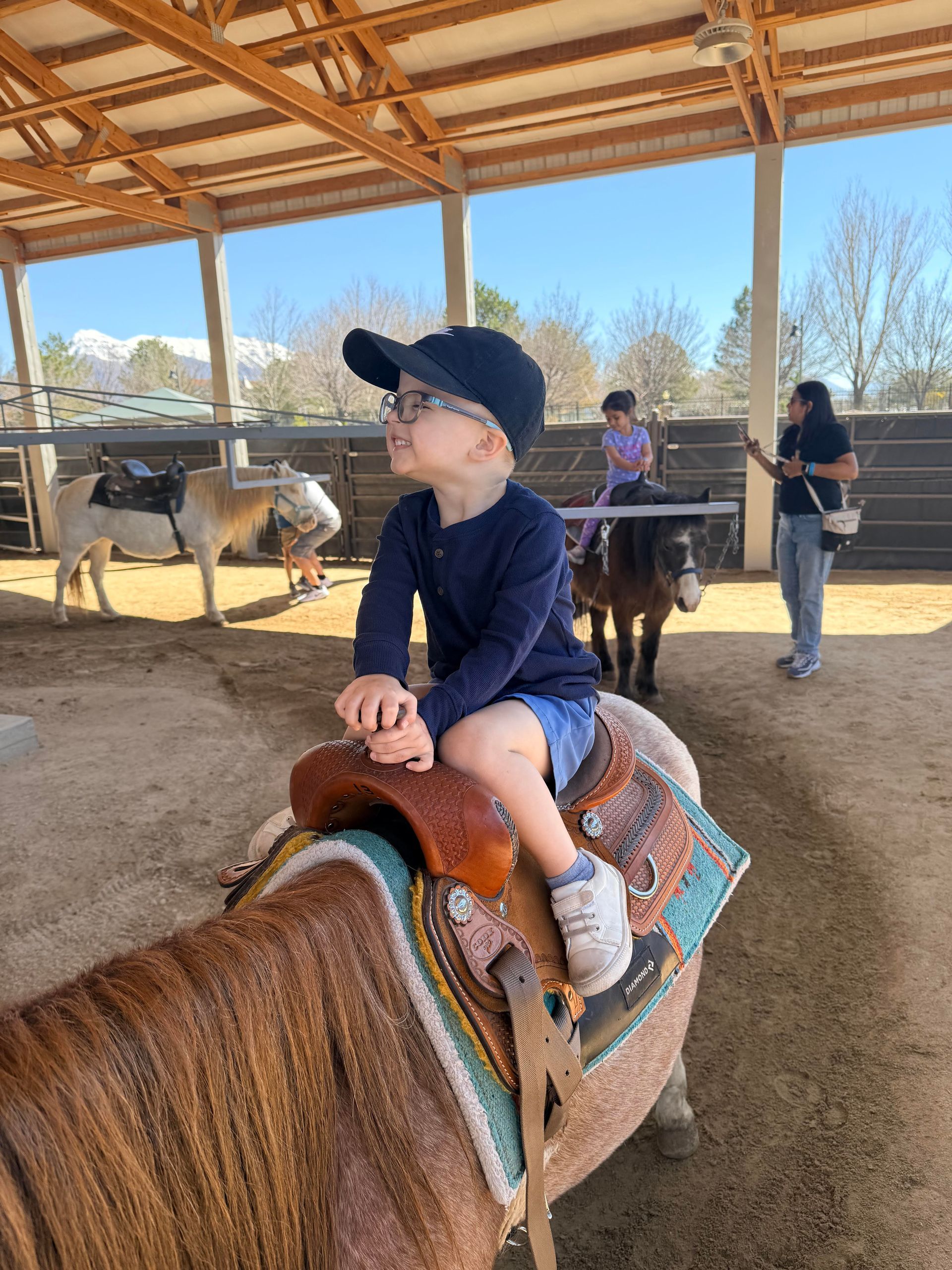 Child riding a horse in a covered arena, wearing a navy cap and shirt.