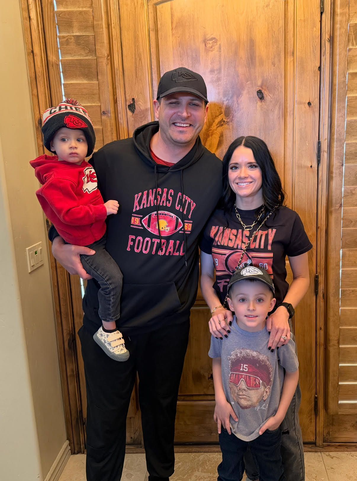 Family of four posing indoors in matching Utah football shirts, standing by a wooden door.