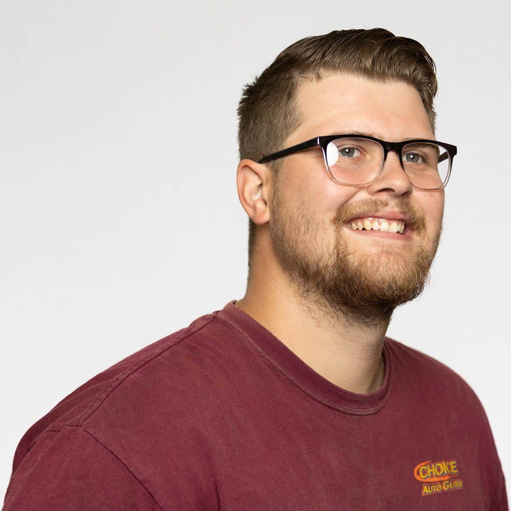 A man wearing glasses and a maroon shirt is smiling