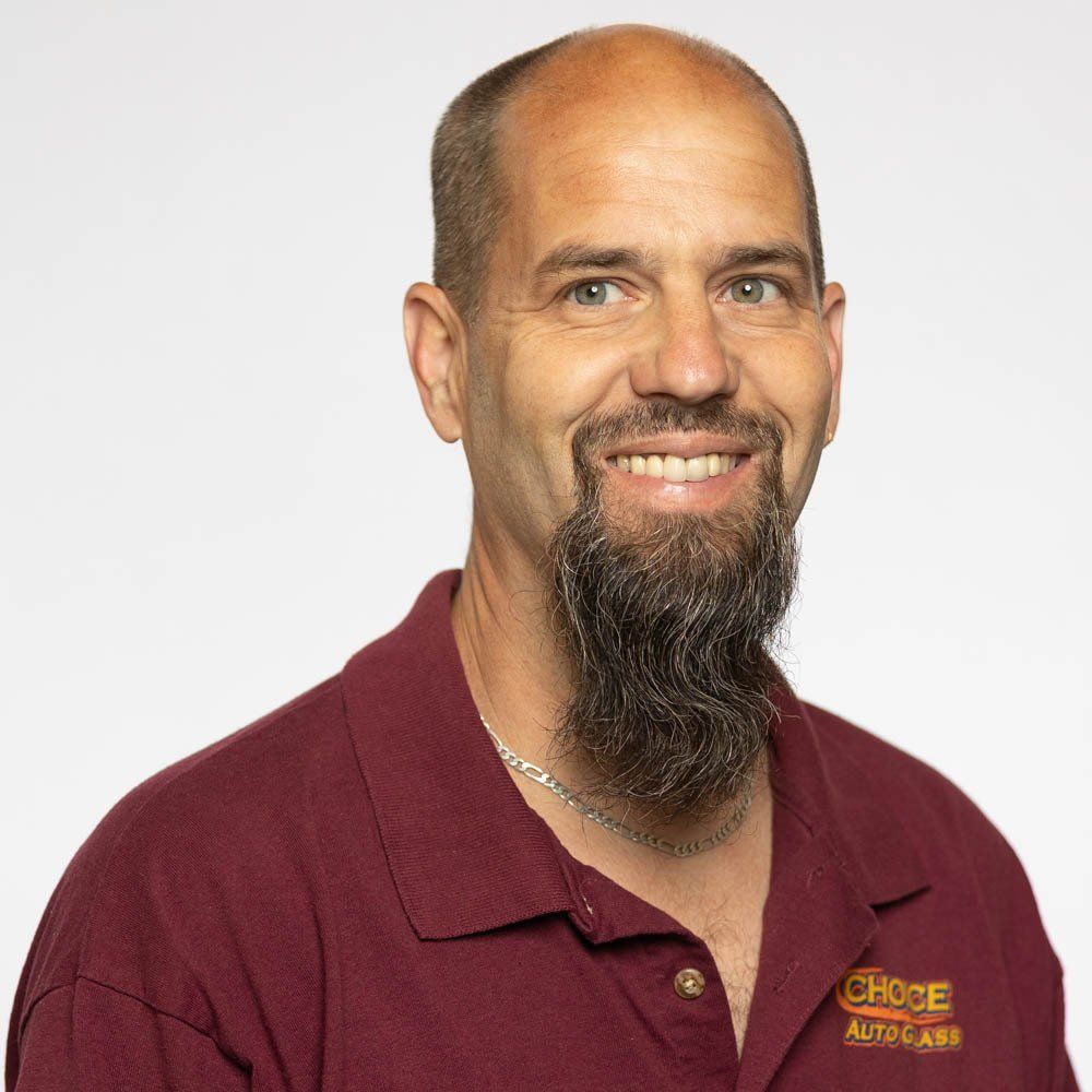 A man with a beard is wearing a maroon shirt and smiling.