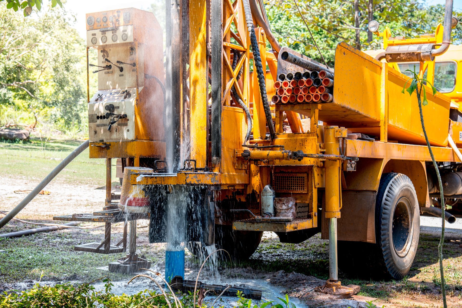 A yellow water well drilling machine operating in a backyard.