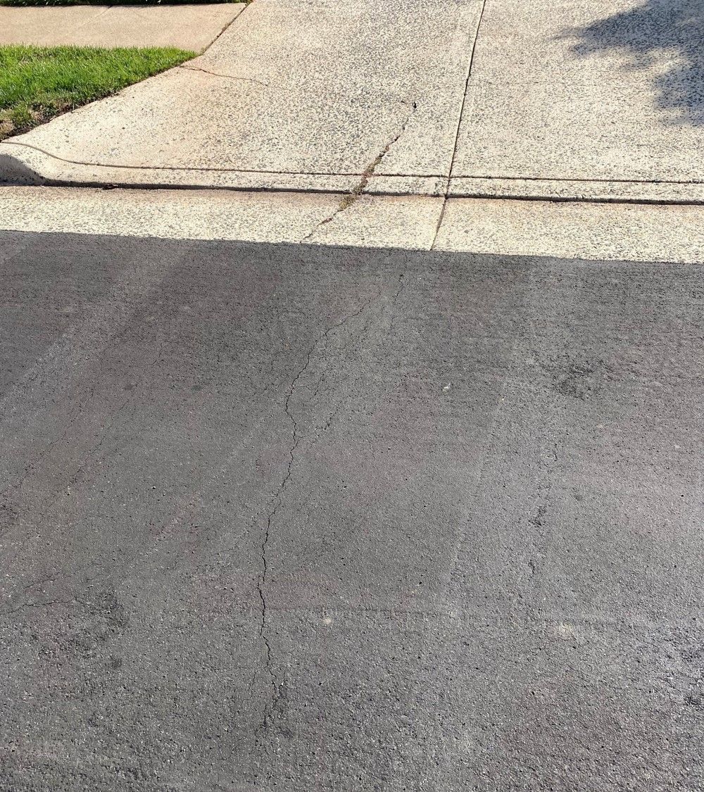 cracks in the road going up into the concrete driveway