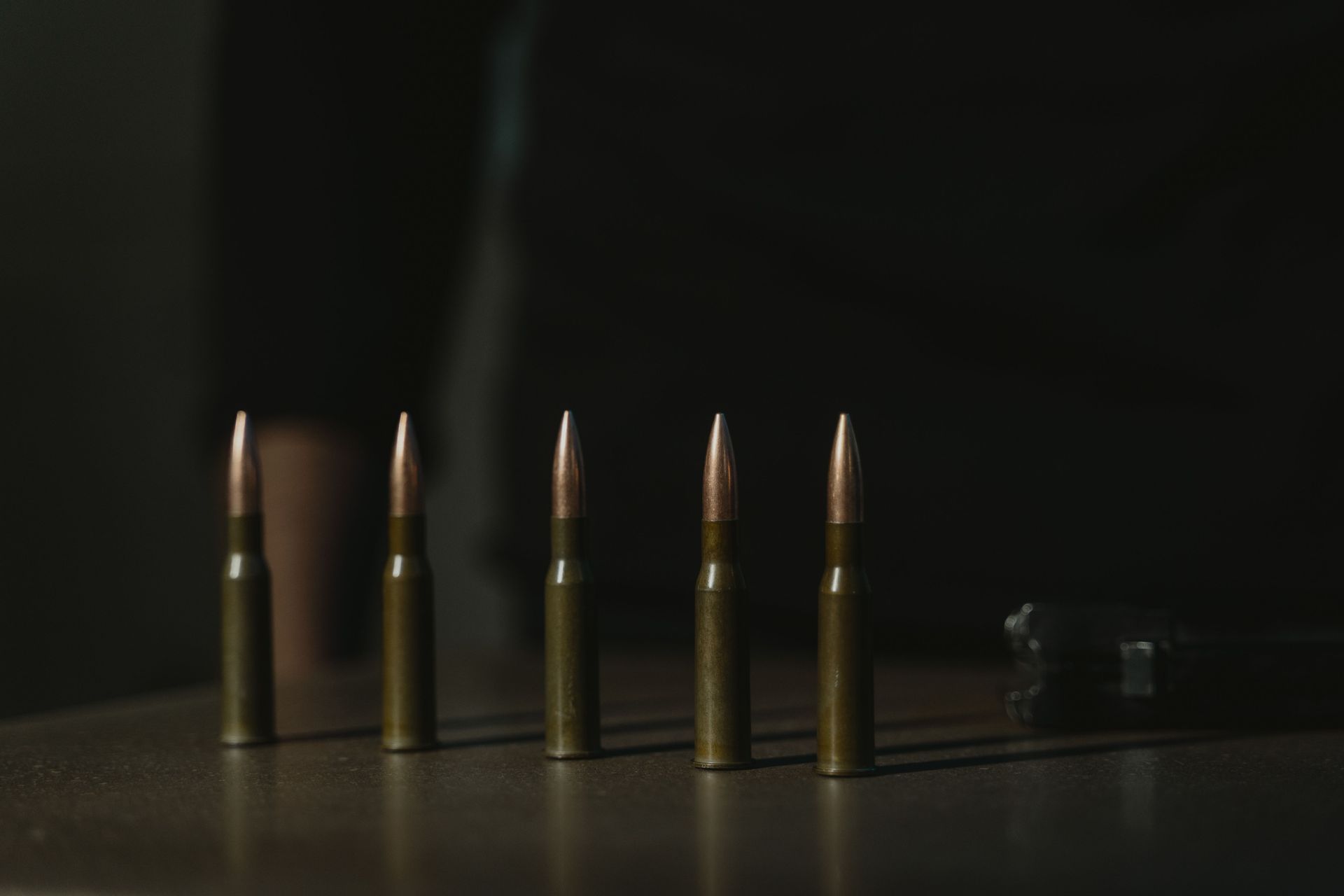 Five rifle cartridges standing upright on a dark surface, with two smaller rounds to the right.