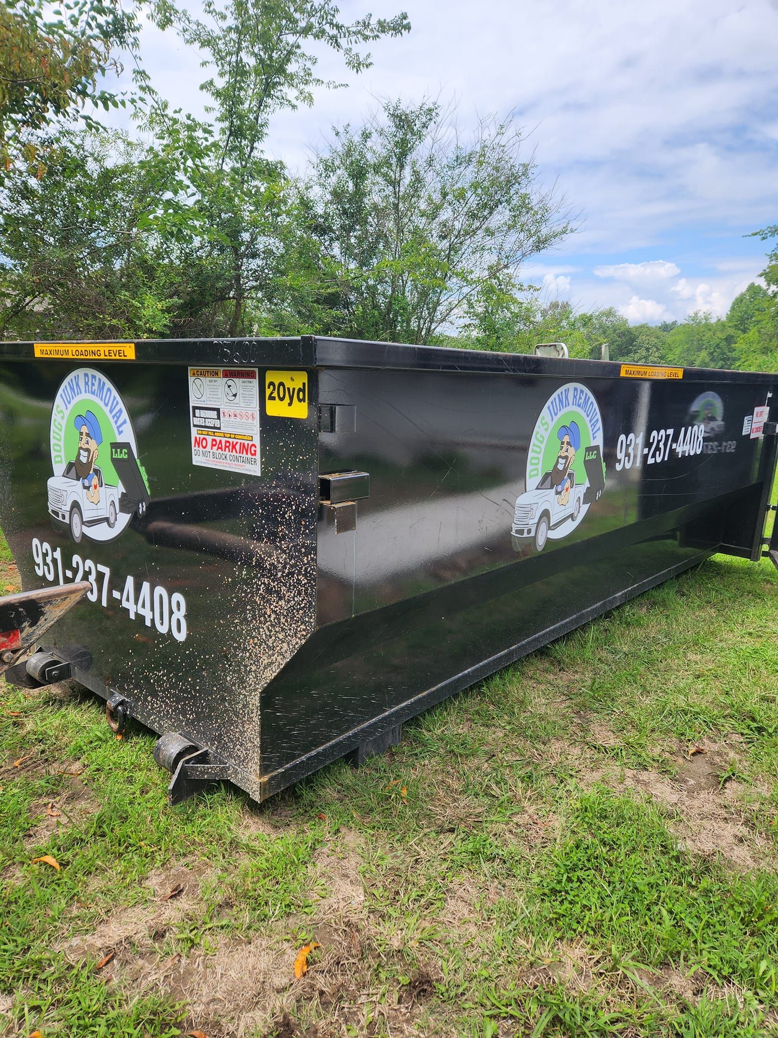 Black dumpster with company logo and phone number, sitting on grass.