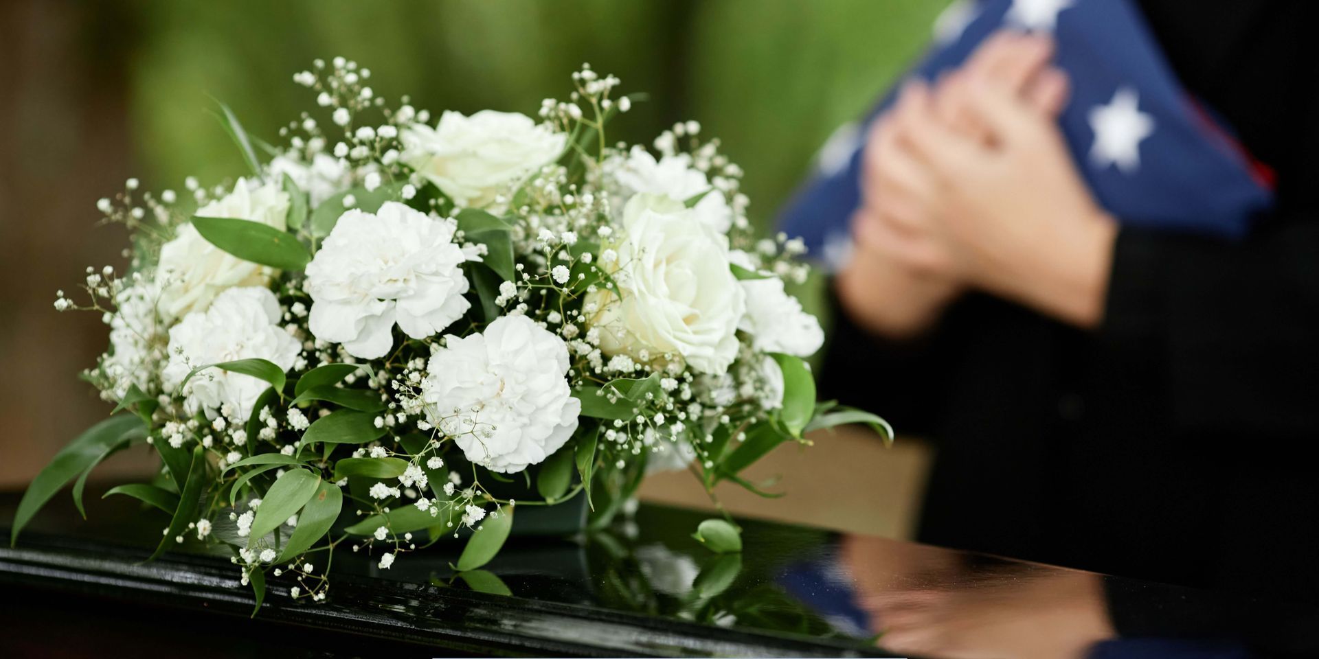 White floral arrangement displayed at a memorial service, with a folded American flag in the background, representing funeral home and cremation care with honor.