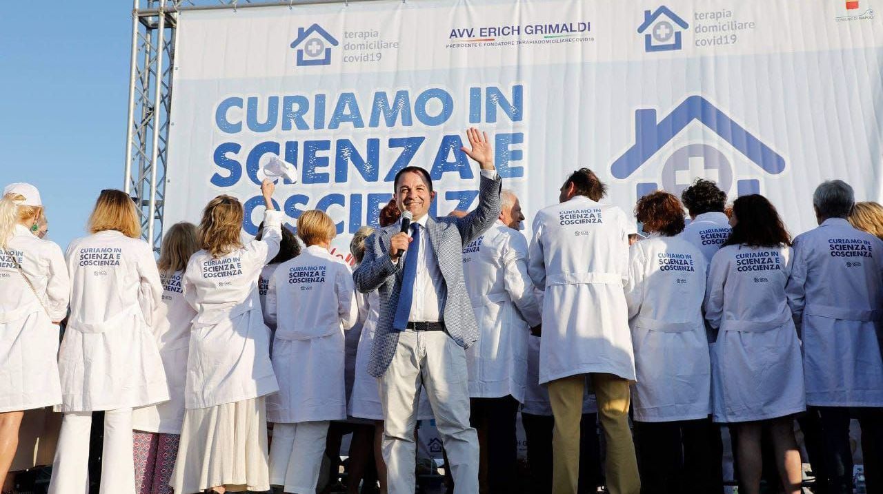 Erich Grimaldi ed un gruppo di medici in piedi davanti a un cartello che dice curiamo in scienza e coscienza