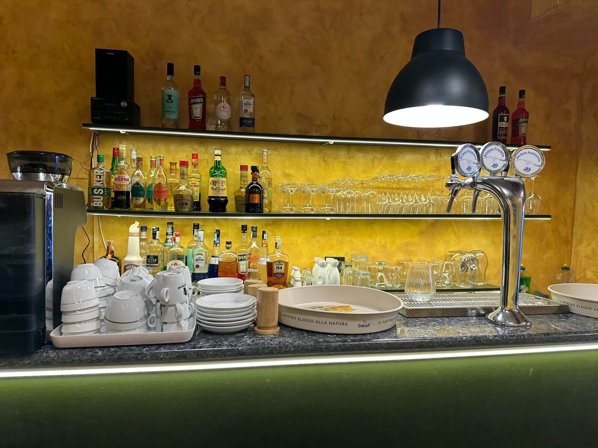 Bancone bar retroilluminato con bottiglie, bicchieri, spillatori e lampade a sospensione
