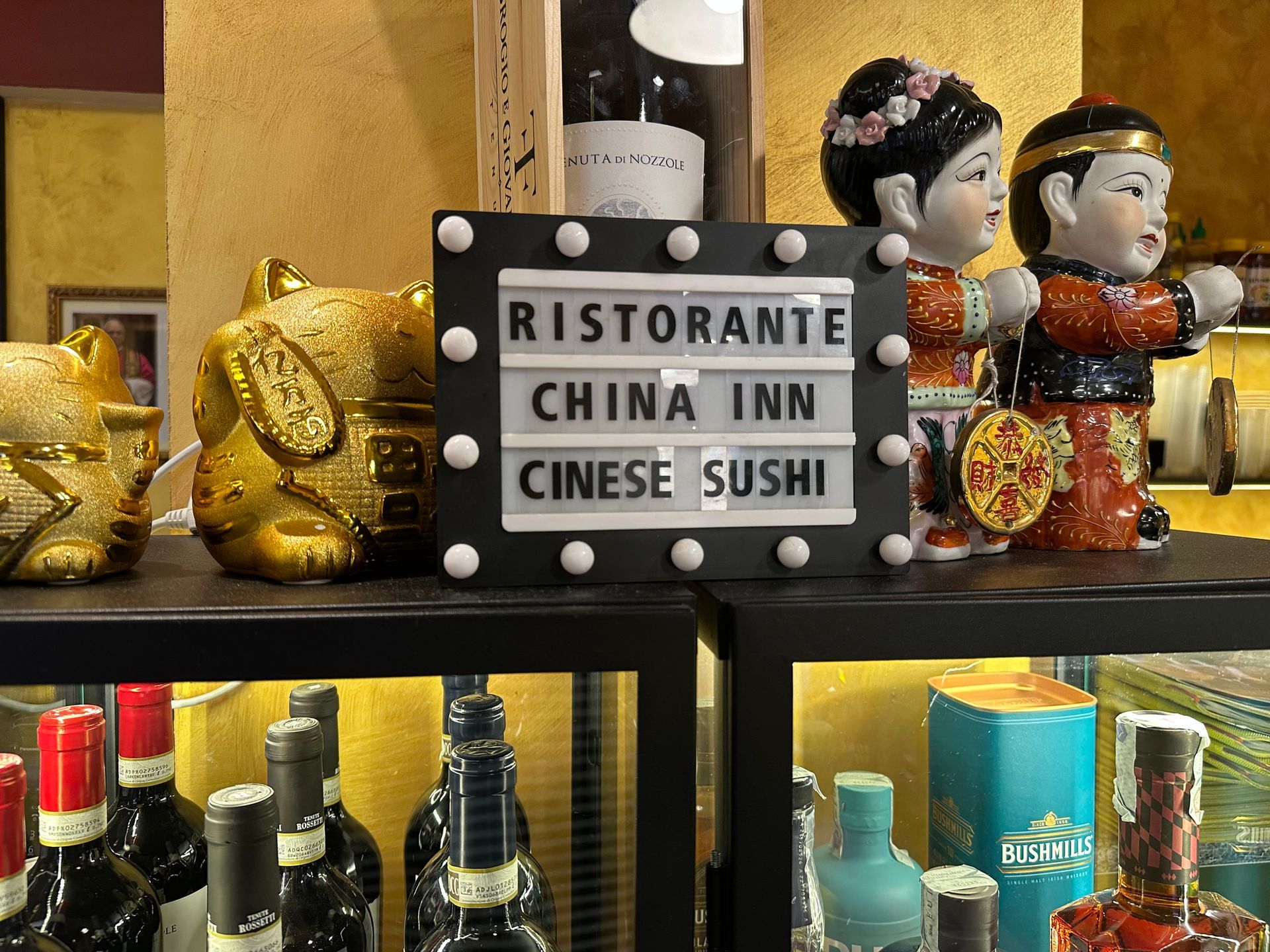 Mensola decorativa di un ristorante con un’insegna con scritto «Ristorante China Inn Chinese Sushi» e bottiglie e statuine tutt’intorno