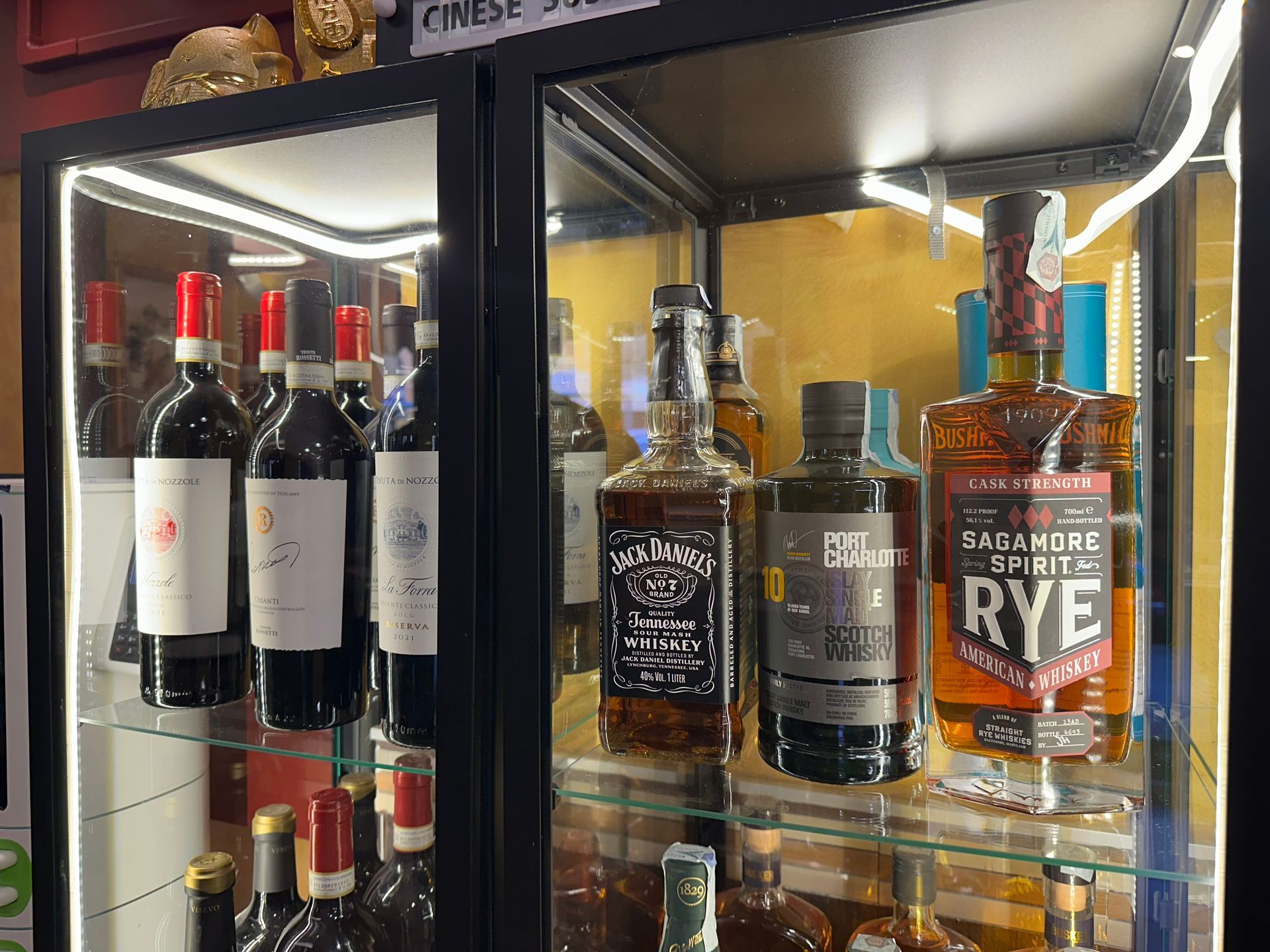 Bottiglie di liquore esposte su ripiani in un frigorifero con porta a vetri.