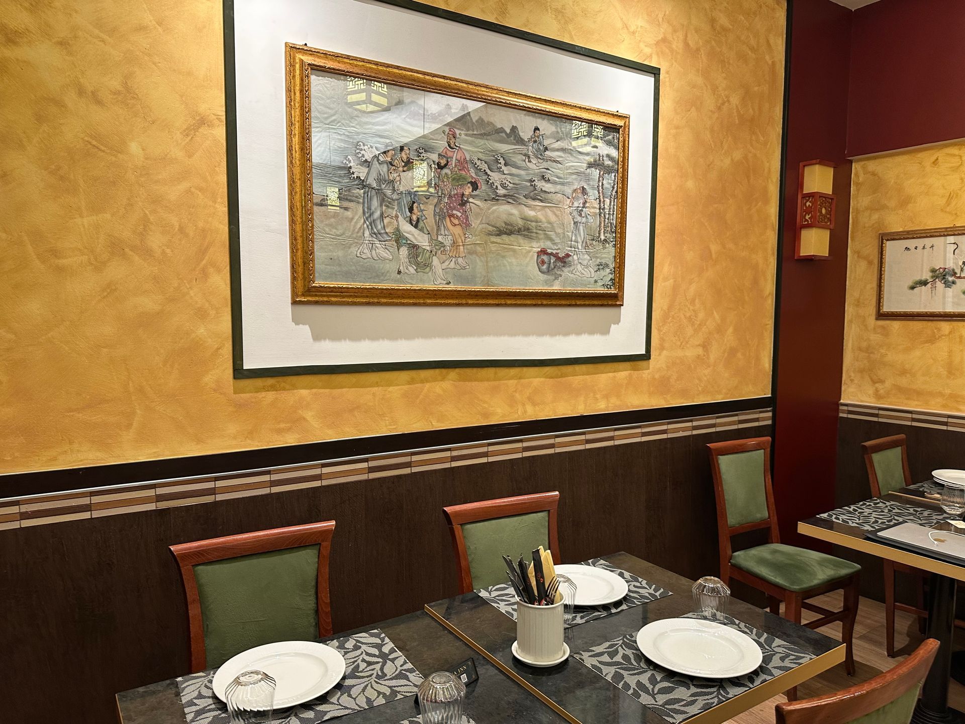 Sala da pranzo vuota di un ristorante, con tavoli apparecchiati, pareti dorate e quadri incorniciati