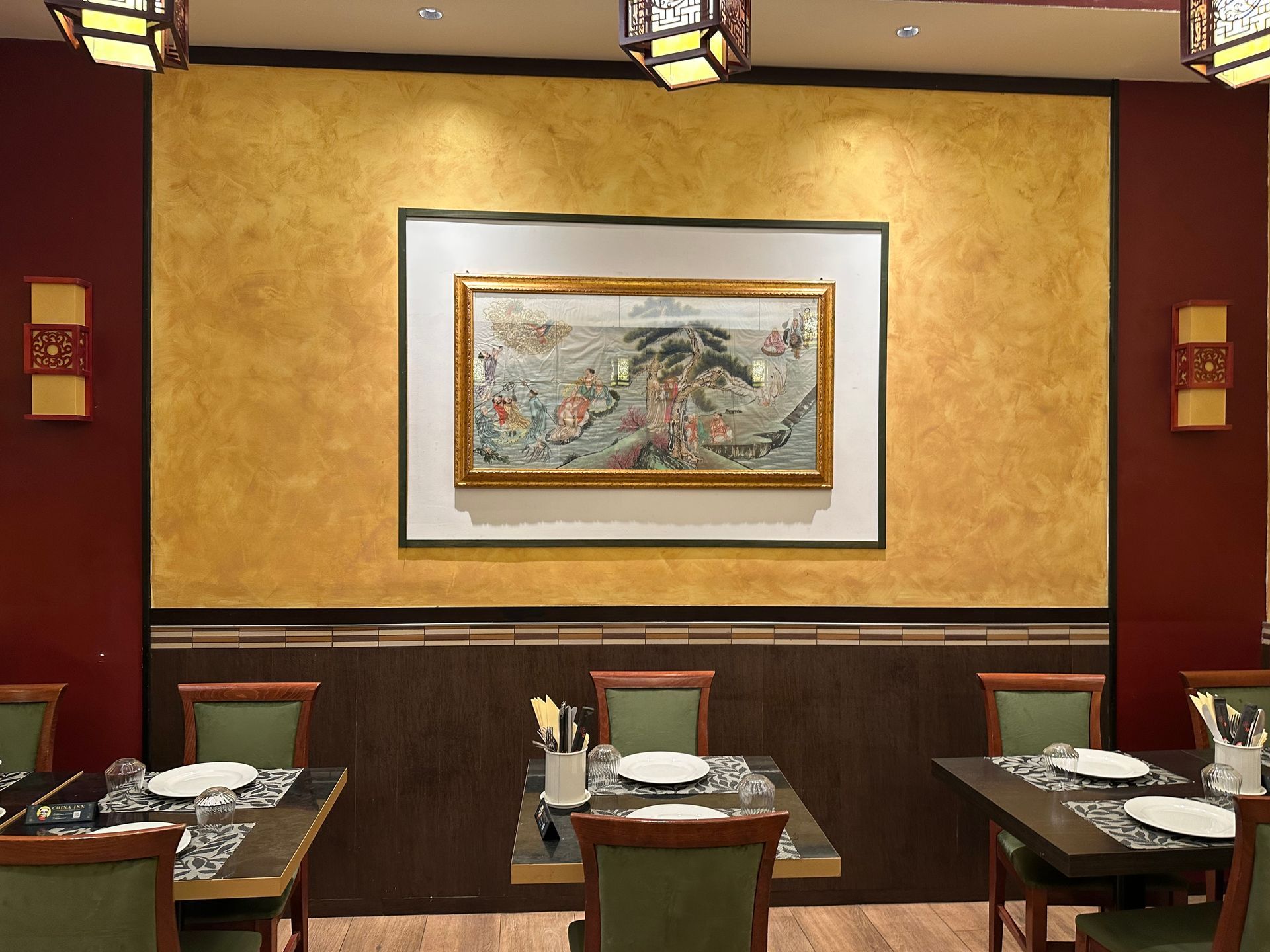 Sala da pranzo vuota di un ristorante, con tavoli, sedie e un quadro incorniciato su una parete dorata