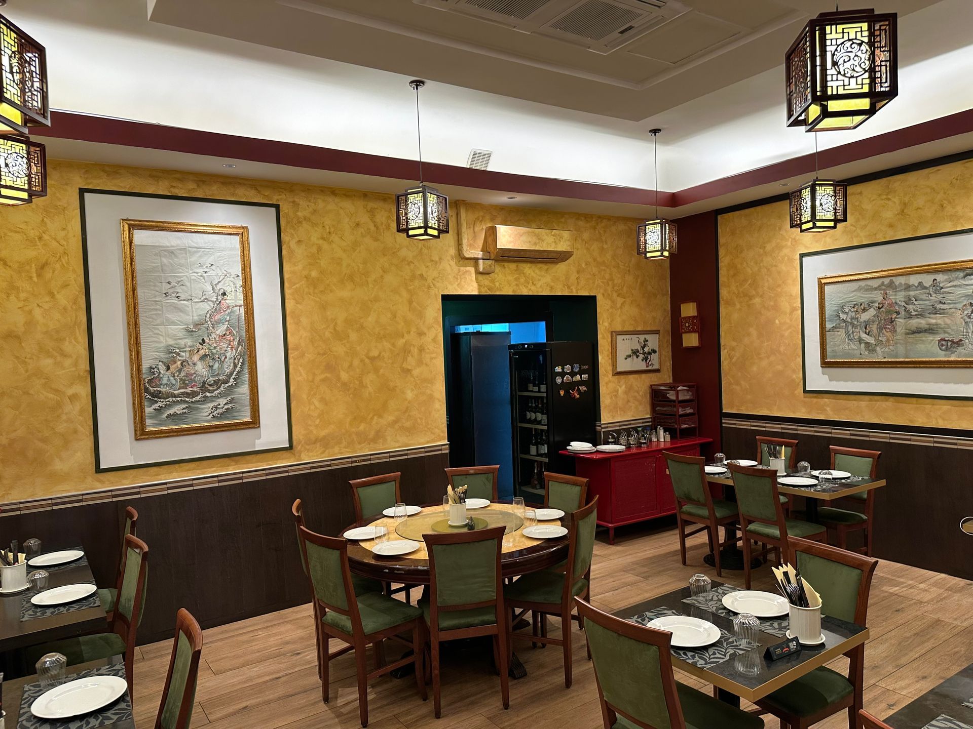Accogliente sala da pranzo di un ristorante con tavoli apparecchiati, lanterne sospese e opere d’arte incorniciate alle pareti dorate
