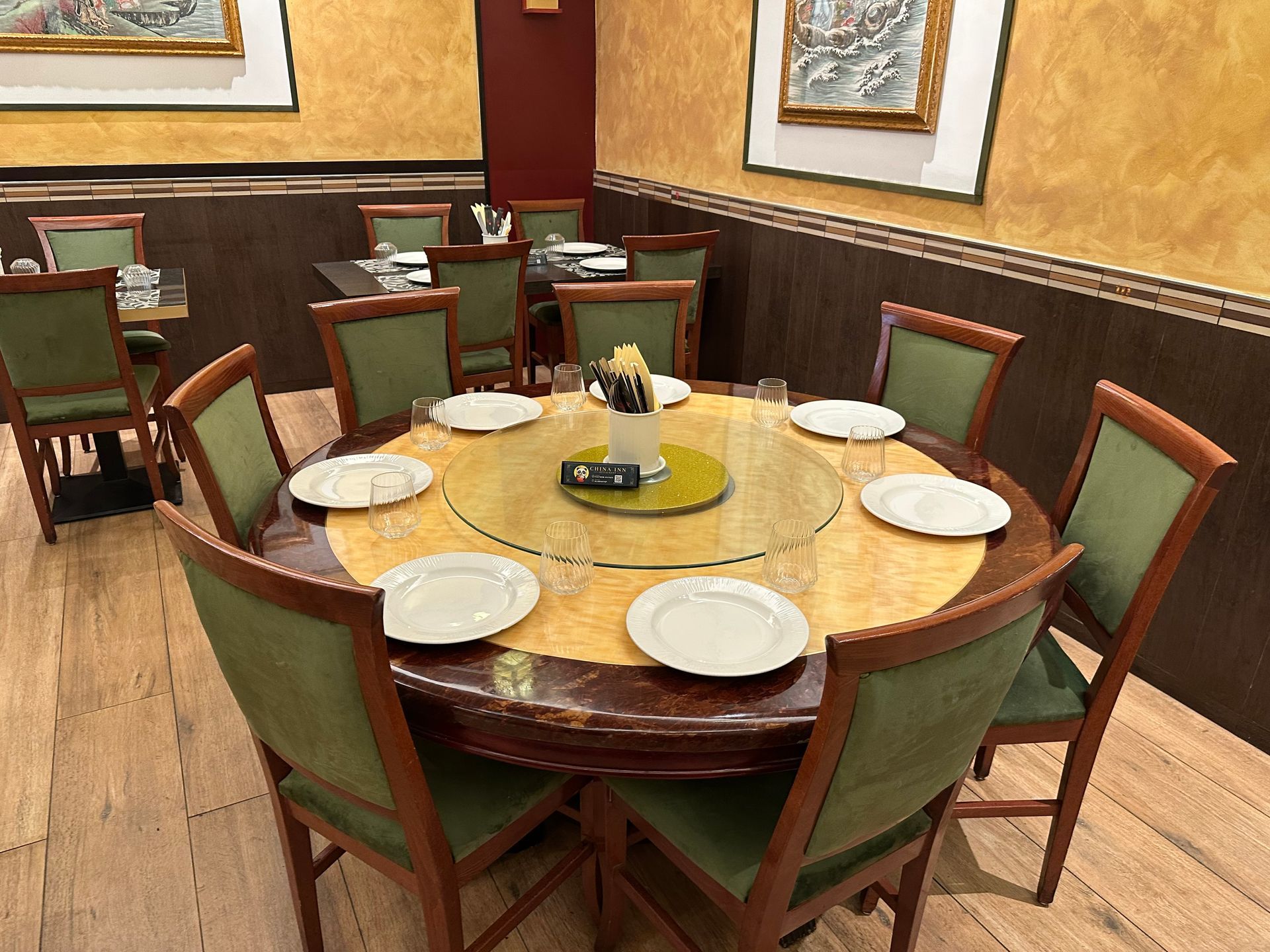Tavolo da pranzo rotondo apparecchiato con piatti bianchi e sedie verdi in una sala ristorante dall’illuminazione calda