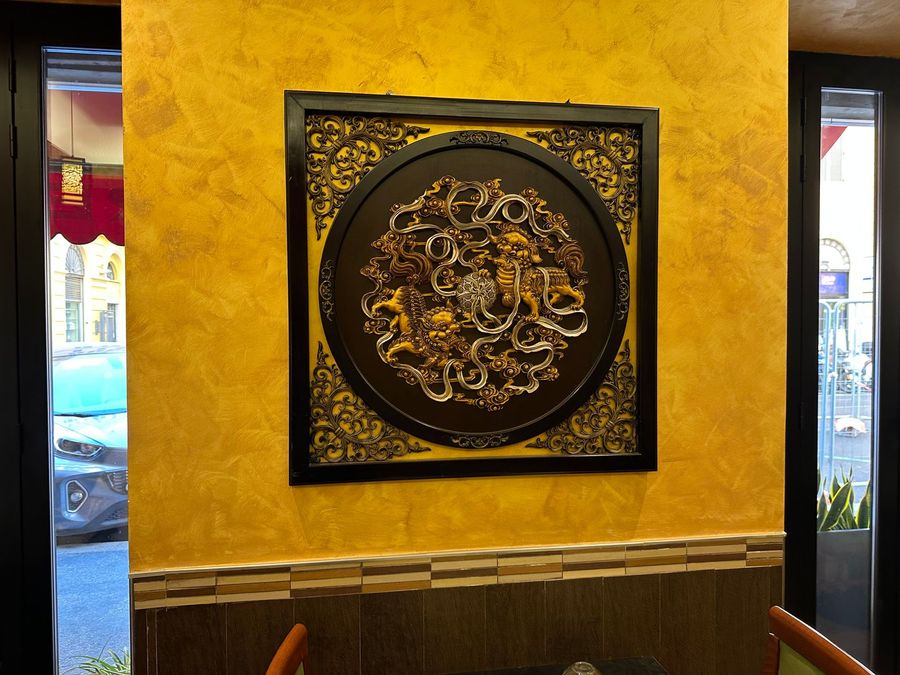 Decorazione murale dorata in rilievo su una parete gialla dalla texture materica, in un corridoio interno poco illuminato