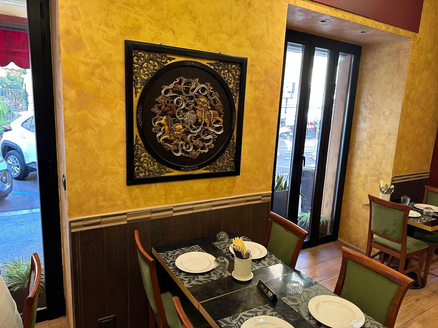 Piccolo tavolo da ristorante vicino a una finestra, con sedie, stoviglie e un elemento decorativo da parete su una parete gialla.