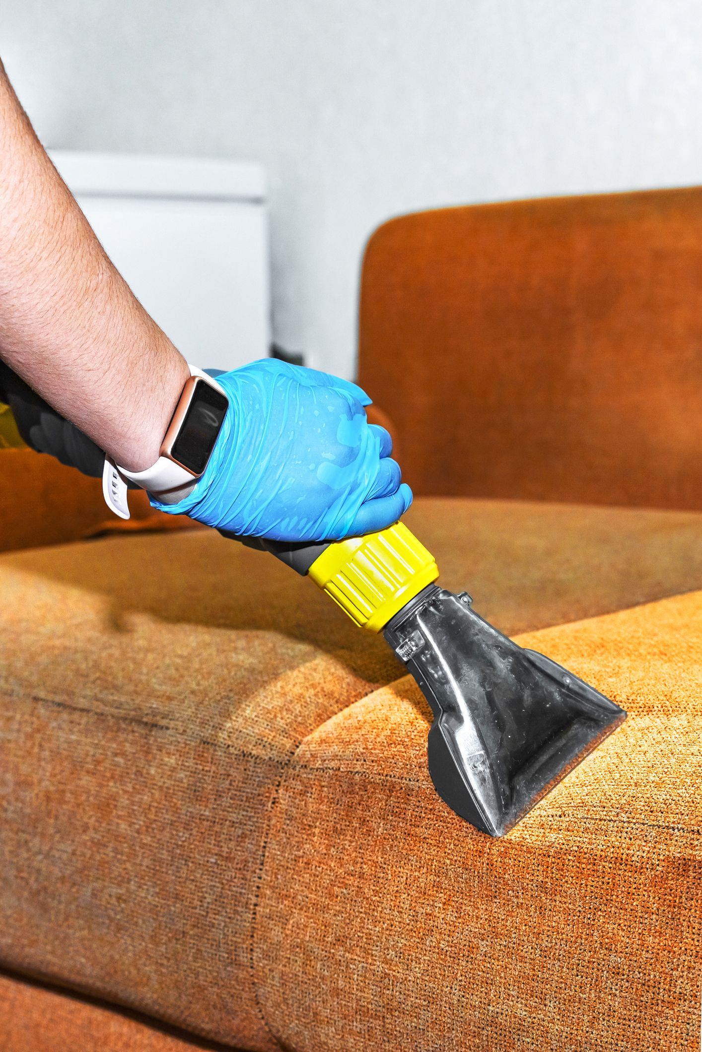A person is cleaning a couch with a vacuum cleaner.
