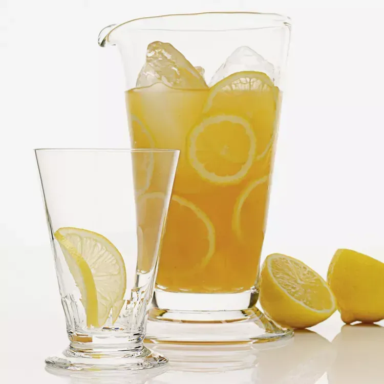 A pitcher of lemonade next to a glass with lemon slices in it