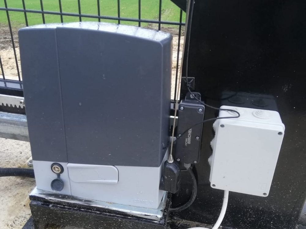 Close-up of an electric gate motor and weatherproof control box mounted at the base of a gate post