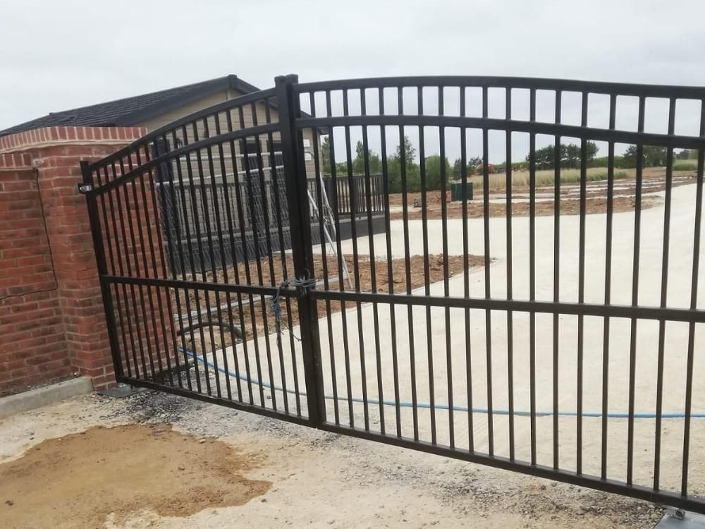 Black metal railing electric gates hung between brick pillars on a newly laid driveway