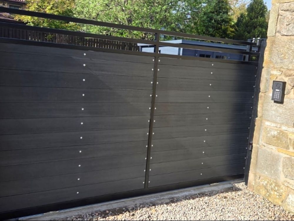 Anthracite slatted composite electric gates with keypad entry mounted on a stone pillar