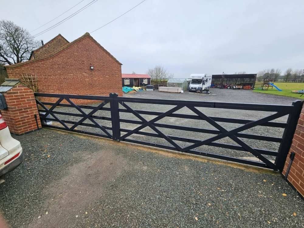 Black metal five-bar style electric gate across a wide gravel entrance