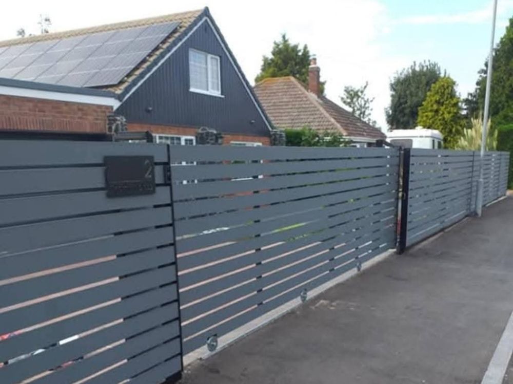 Grey horizontal slat electric gates with matching boundary fencing along a driveway