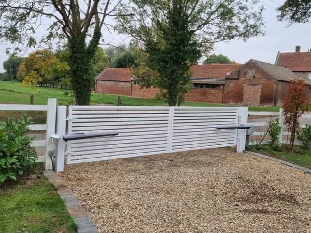 White estate-style electric gates and matching post and rail fencing at a rural entrance