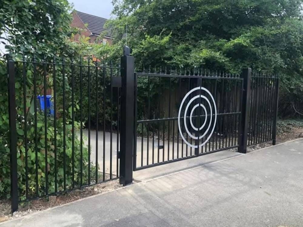 Black metal electric driveway gate with matching pedestrian gate and circular spiral detail