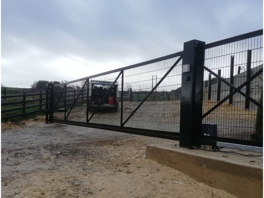 Black metal electric sliding gate part-way open across a gravel driveway entrance