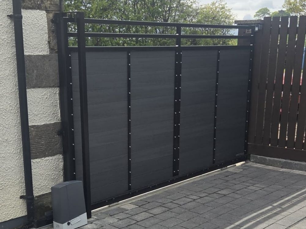 Anthracite composite sliding electric gate with visible sliding motor on a block paved driveway