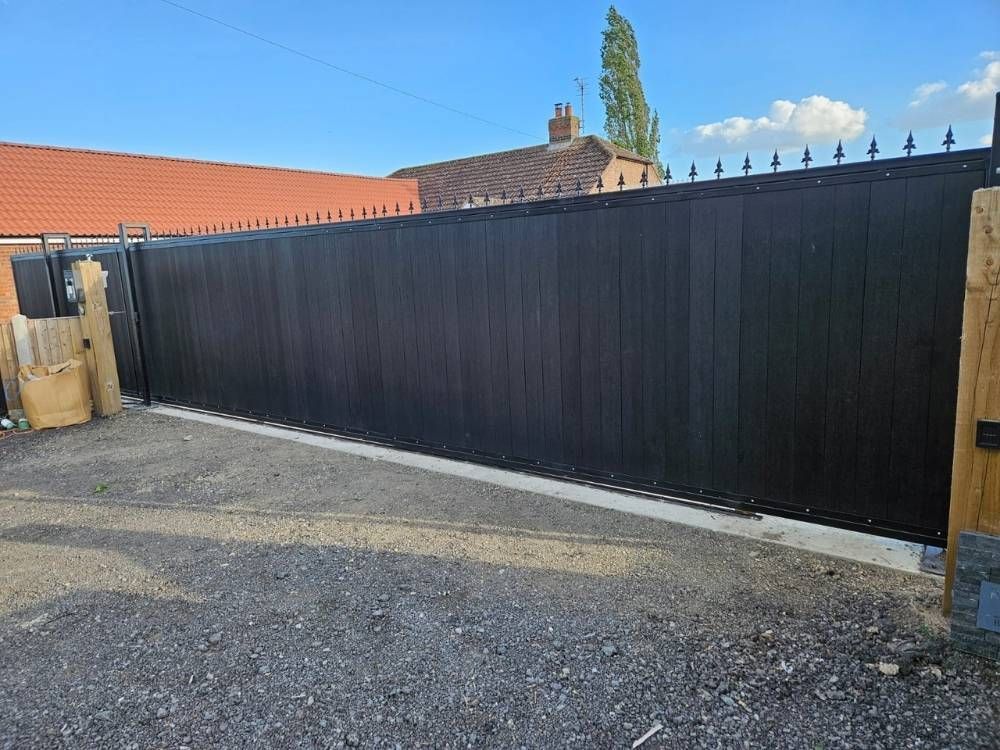 Composite electric sliding gate with fleur-de-lis detail between brick pillars