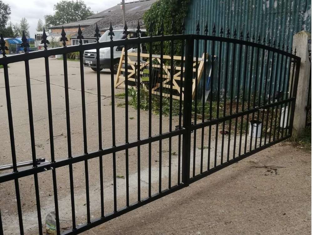 Black metal bow-top electric swing gates with vertical bar infill on a gravel driveway