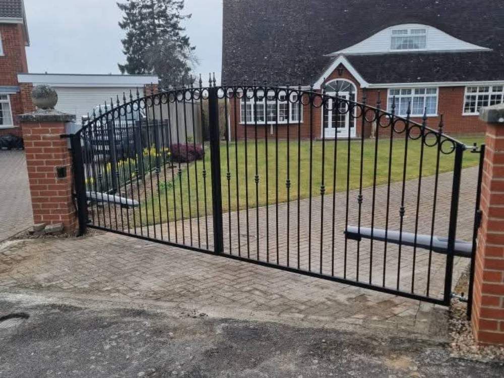 Black metal railing electric swing gates between brick pillars at a bungalow entrance