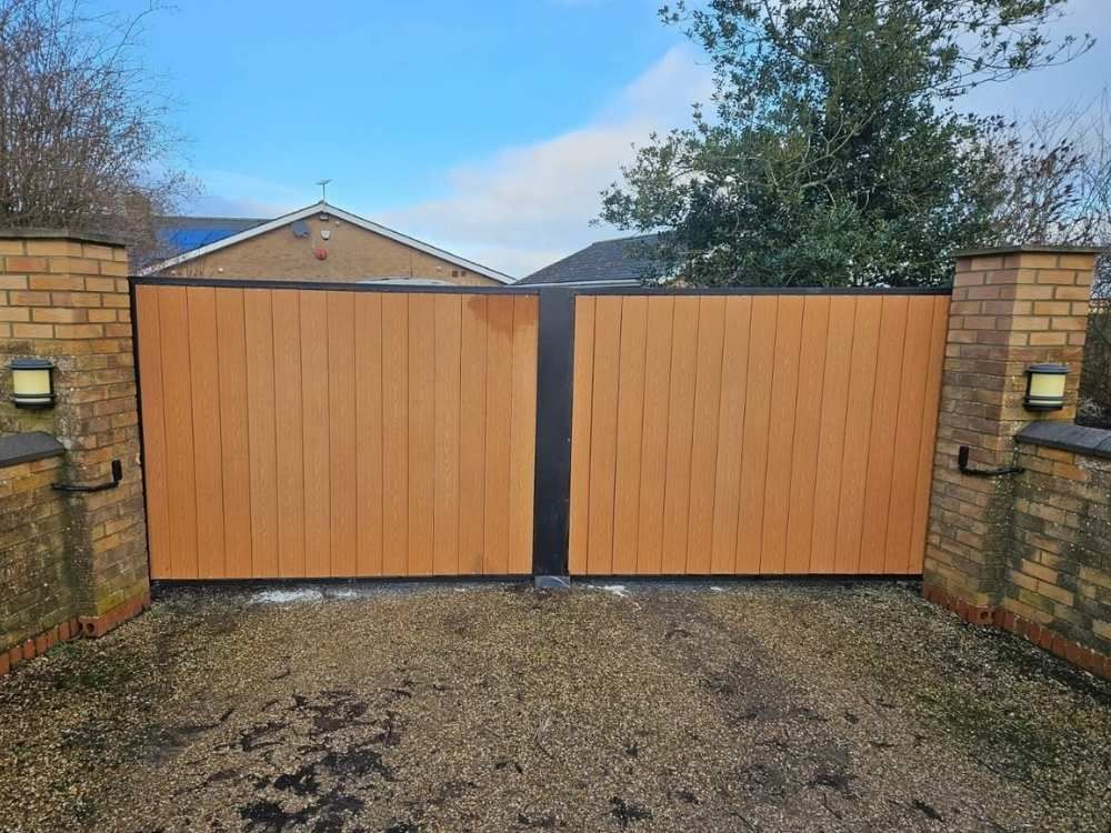 Electric swing gates with vertical timber infill and black frame hung between brick pillars