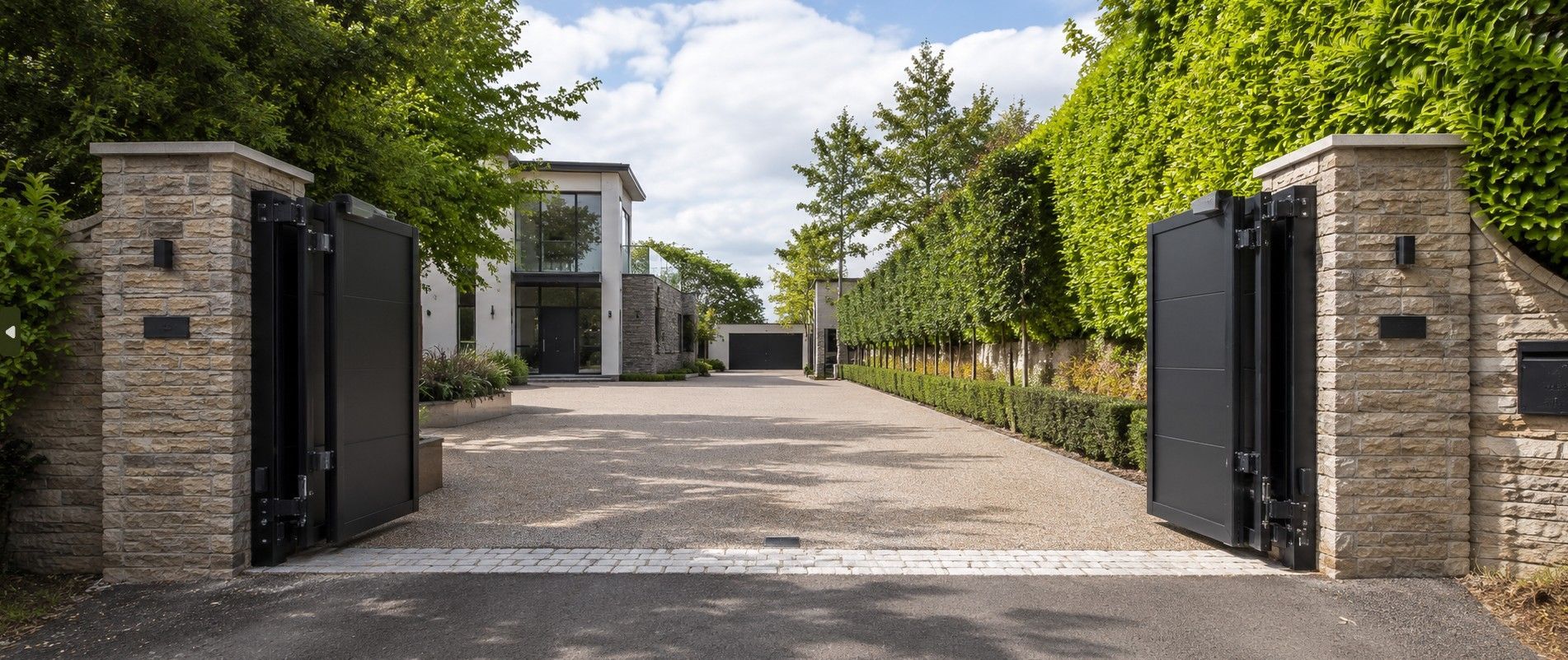 Electric bi-folding gates fully open and folded compactly against pillars at a wide residential entrance