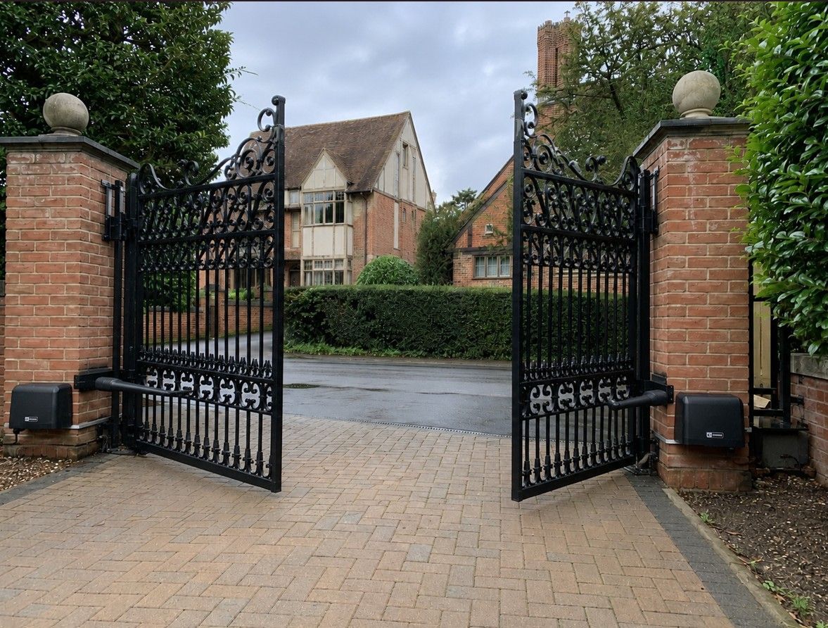 Black wrought iron electric swing gates on brick pillars at a period British home