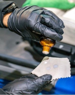 A person wearing black gloves is pouring a liquid into a cloth.