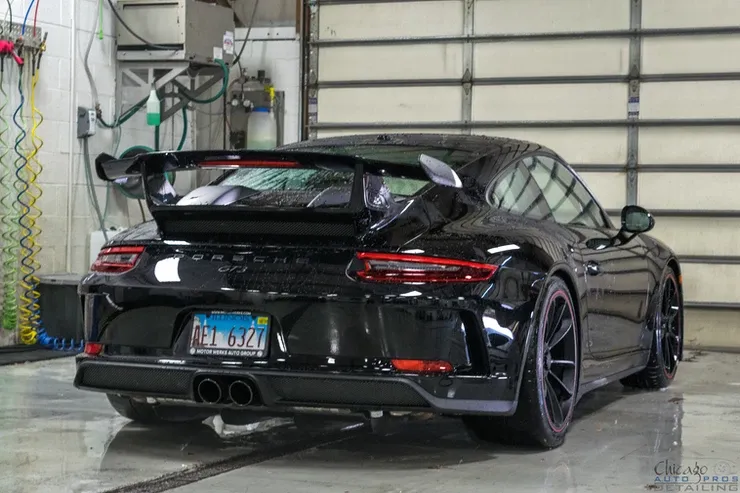 A black porsche 911 gt3 is parked in front of a garage door.