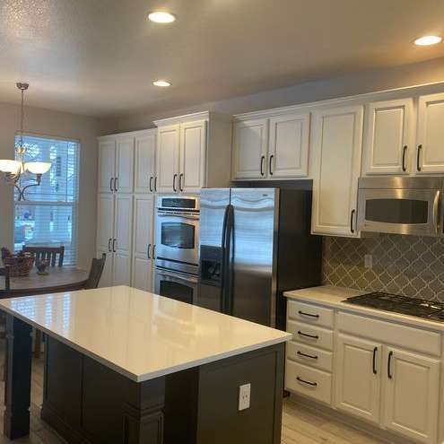 A kitchen with white cabinets , stainless steel appliances , and a large island.