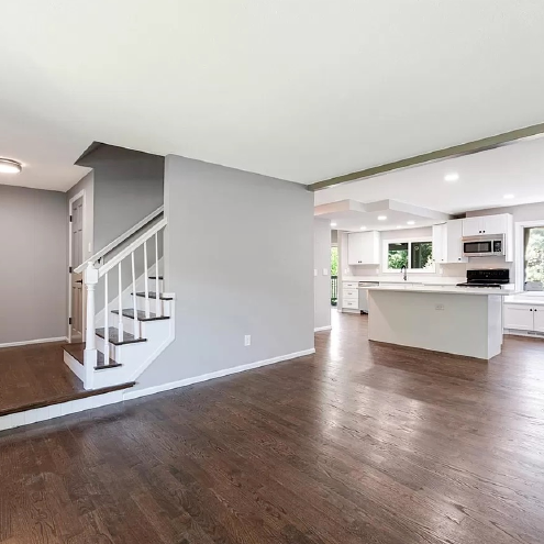 A living room with hardwood floors and stairs leading to a kitchen.
