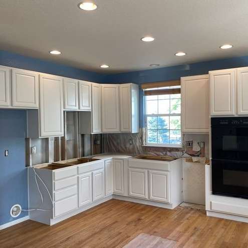 A kitchen with white cabinets , hardwood floors , and a window.