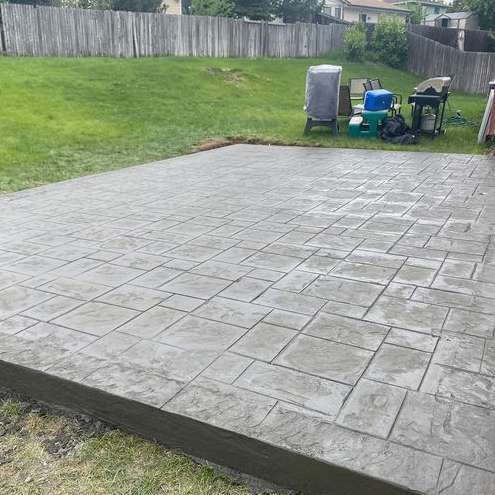 A concrete patio with a grill and chairs in the backyard.