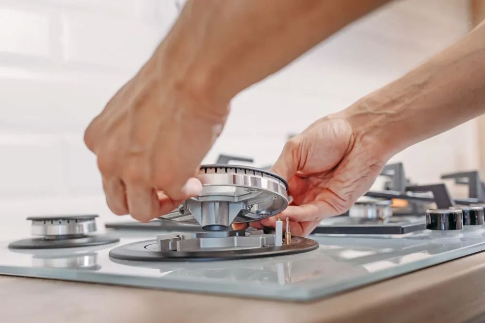 Hands Adjusting a Stove Burner Knob on a Modern Gas Cooktop — The Plumbing & Drainage Co. in Mittagong, NSW
