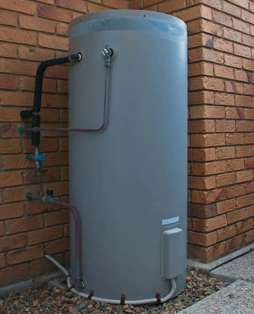 Gray Cylindrical Water Heater Tank Beside a Brick Wall, With Pipes and Valves — The Plumbing & Drainage Co. in Mittagong, NSW