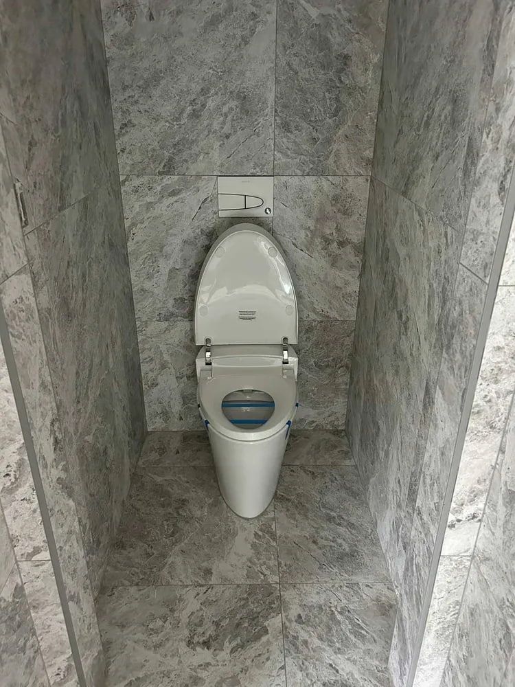 Toilet in a Narrow Gray-tiled Stall With the Seat and Lid Open — The Plumbing & Drainage Co. in Southern Highlands, NSW