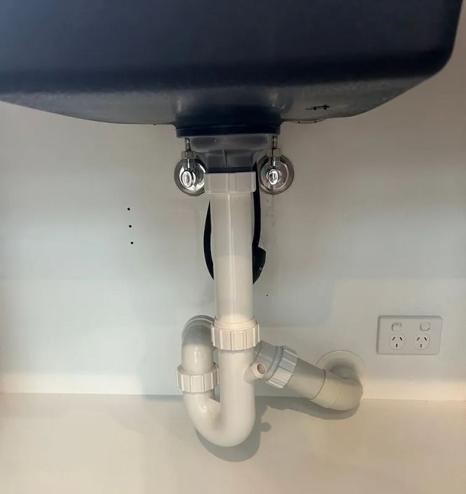 Bathroom Sink Drain Pipes Under a White Sink, With Chrome Water — The Plumbing & Drainage Co. in Mittagong, NSW