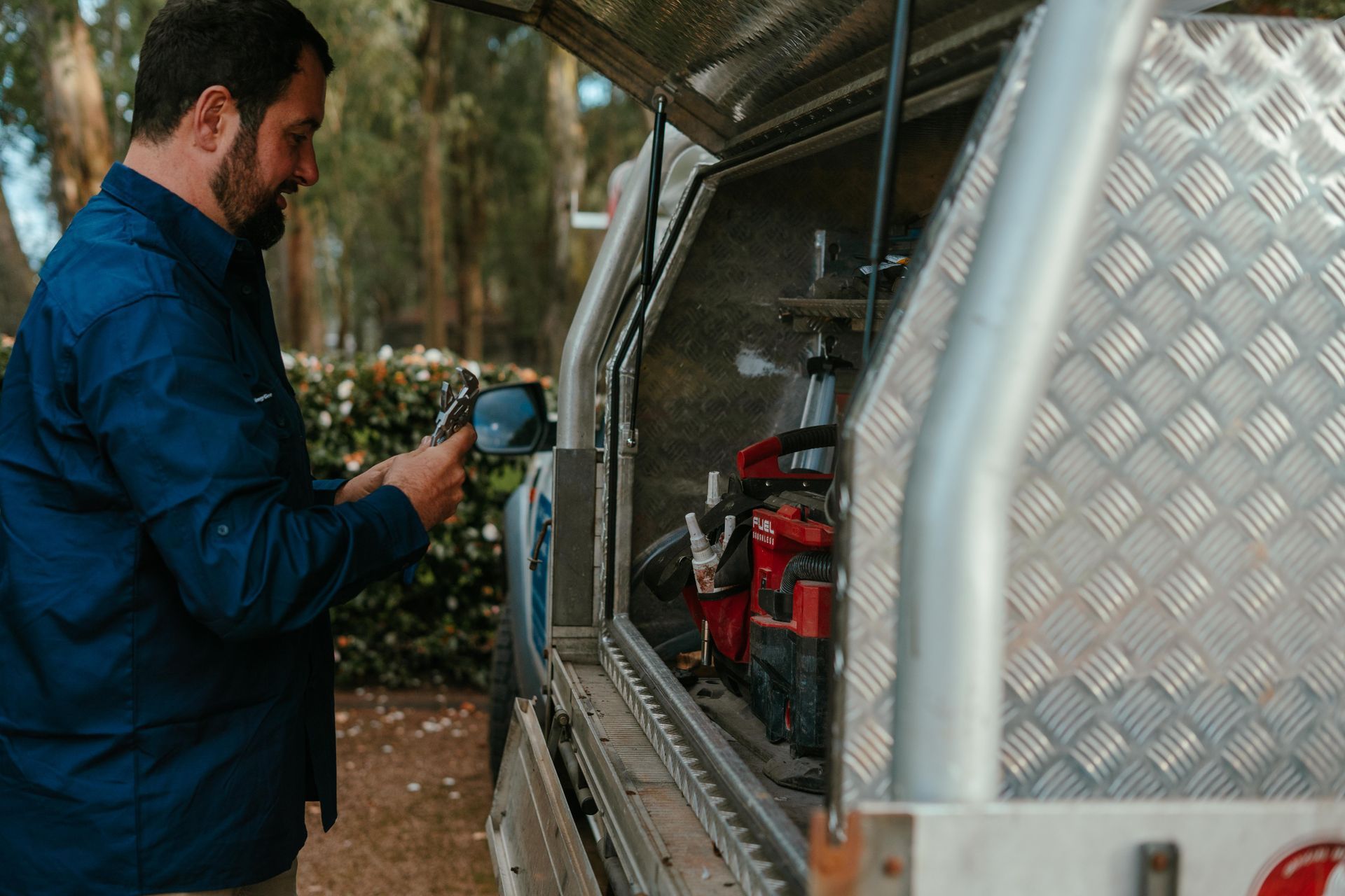 Man in blue jacket spraying equipment in a metal utility trailer outdoors — The Plumbing & Drainage Co. in Southern Highlands, NSW