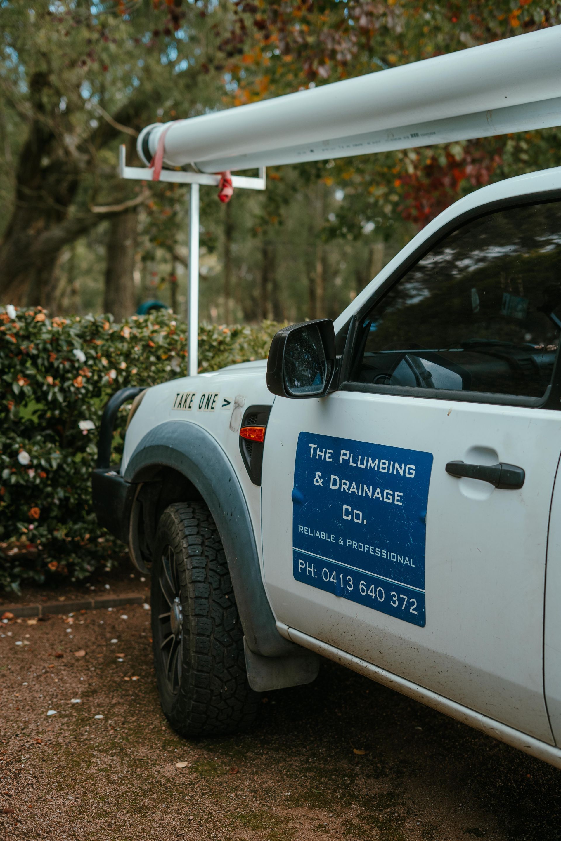 White utility truck parked outdoors with a blue company sign on the door and a roof-mounted beam. — The Plumbing & Drainage Co. in Mittagong, NSW